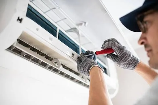 Technician checking airflow at a wall-mounted HVAC unit